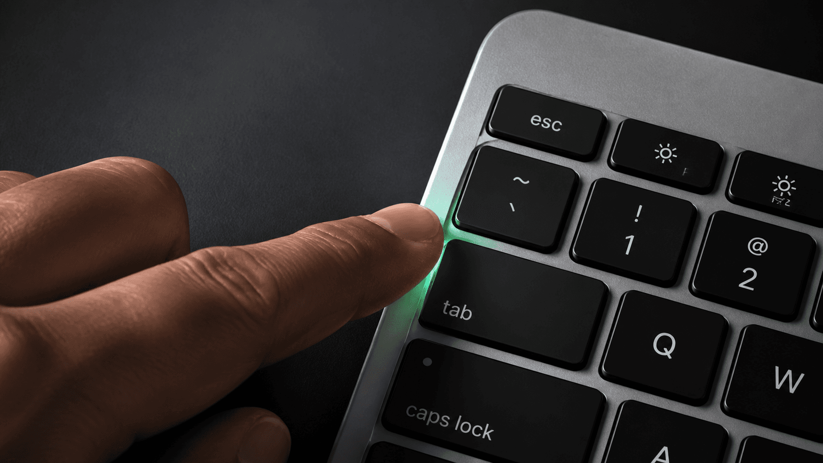 Close-up of a hand pressing the Tab key on a Mac keyboard with a subtle green glow