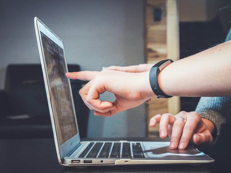 Person using a laptop while another hand points at the screen