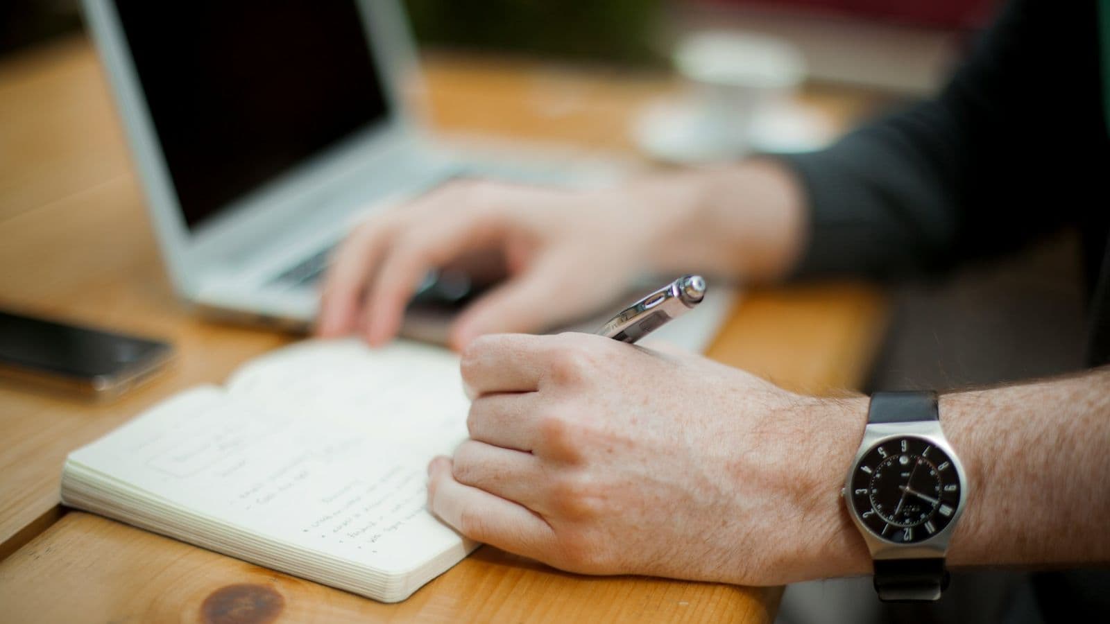 Writer using a notebook beside a laptop