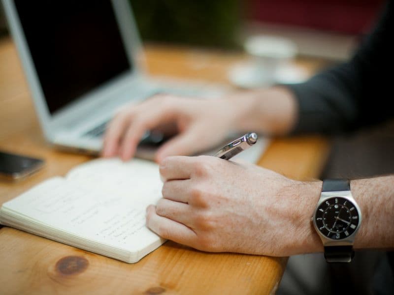 Writer using a notebook beside a laptop