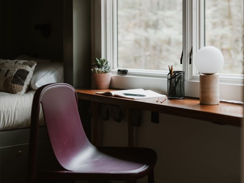 A chair and desk by a window with a lamp.