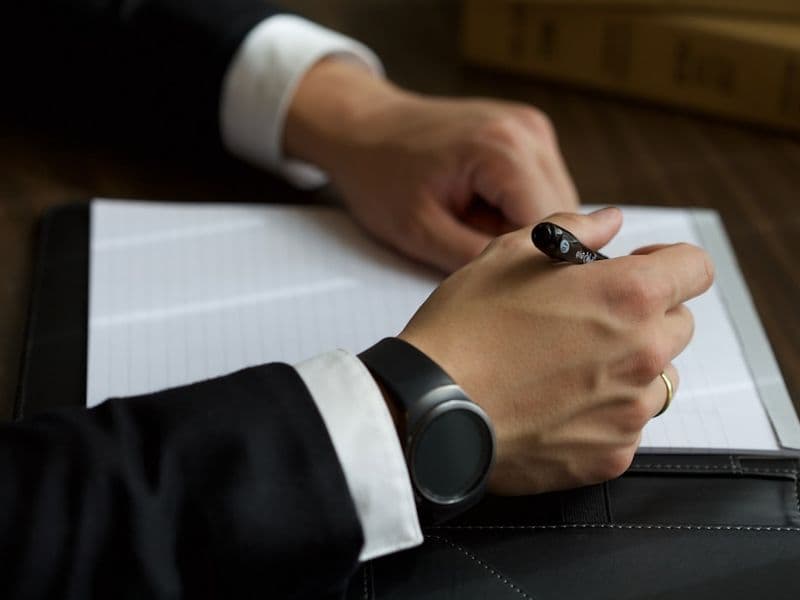 A person in a suit writing on a document.