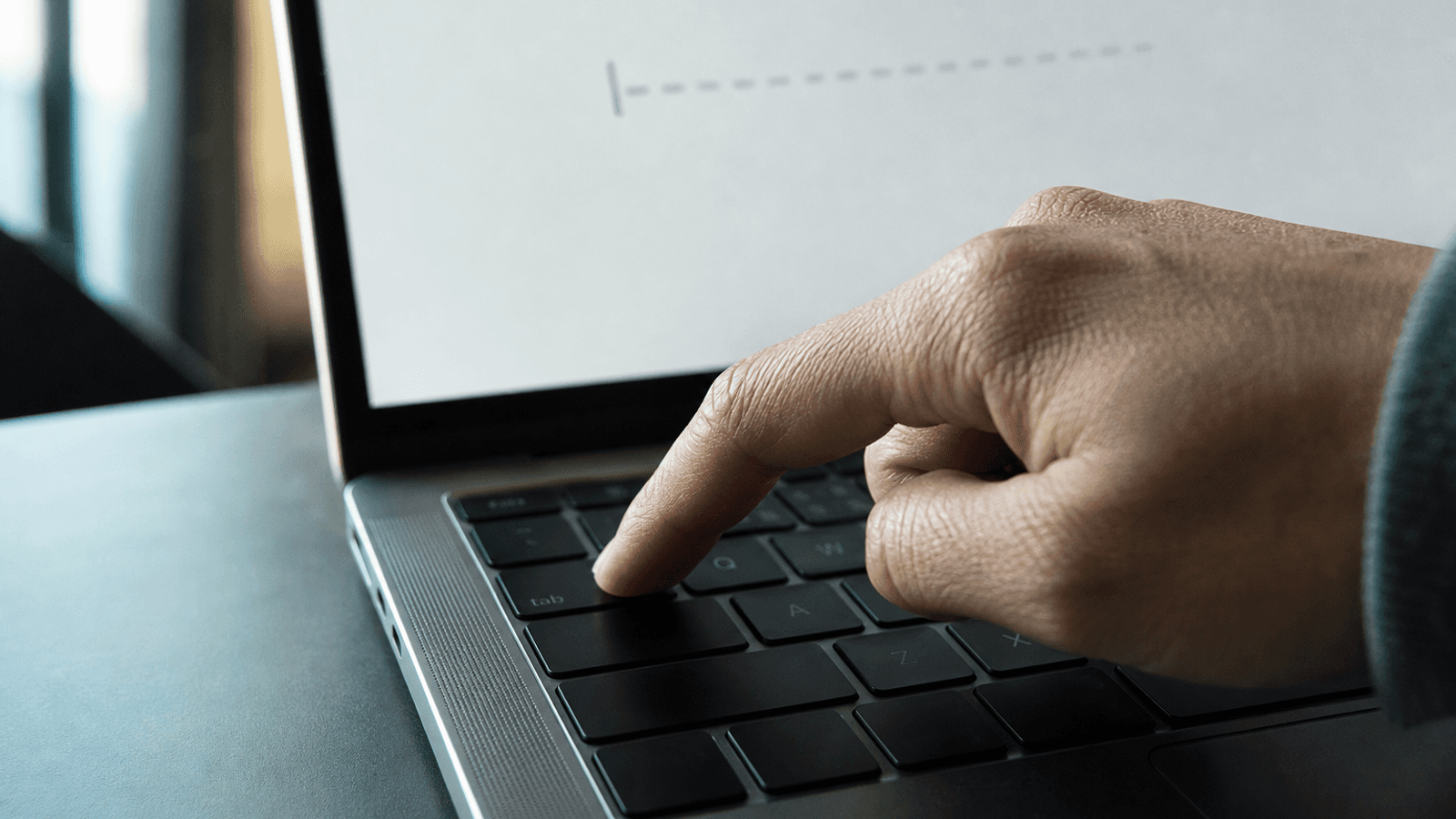 A close-up of a hand pressing the Tab key on a MacBook while a faint autocomplete suggestion appears on screen