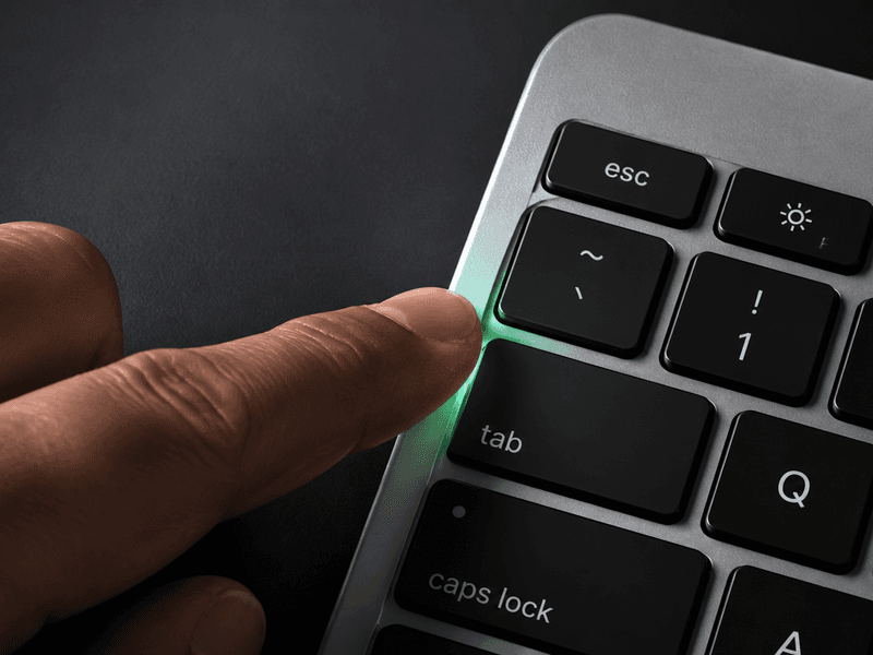 Close-up of a hand pressing the Tab key on a Mac keyboard with a subtle green glow