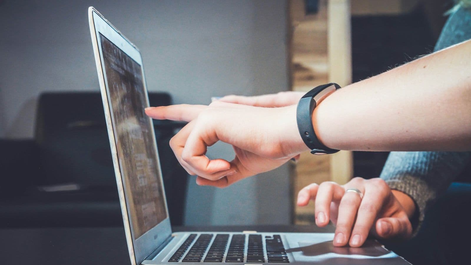 Person using a laptop while another hand points at the screen