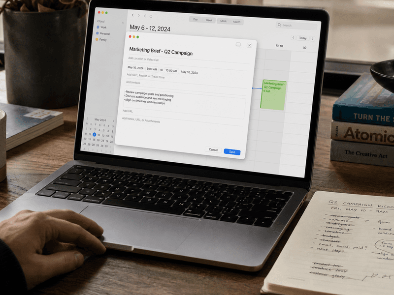 Calendar invite being written on a MacBook with agenda notes beside it